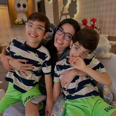 Dra. Graziele Alvim abraçada com duas crianças no consultório de odontopediatria.