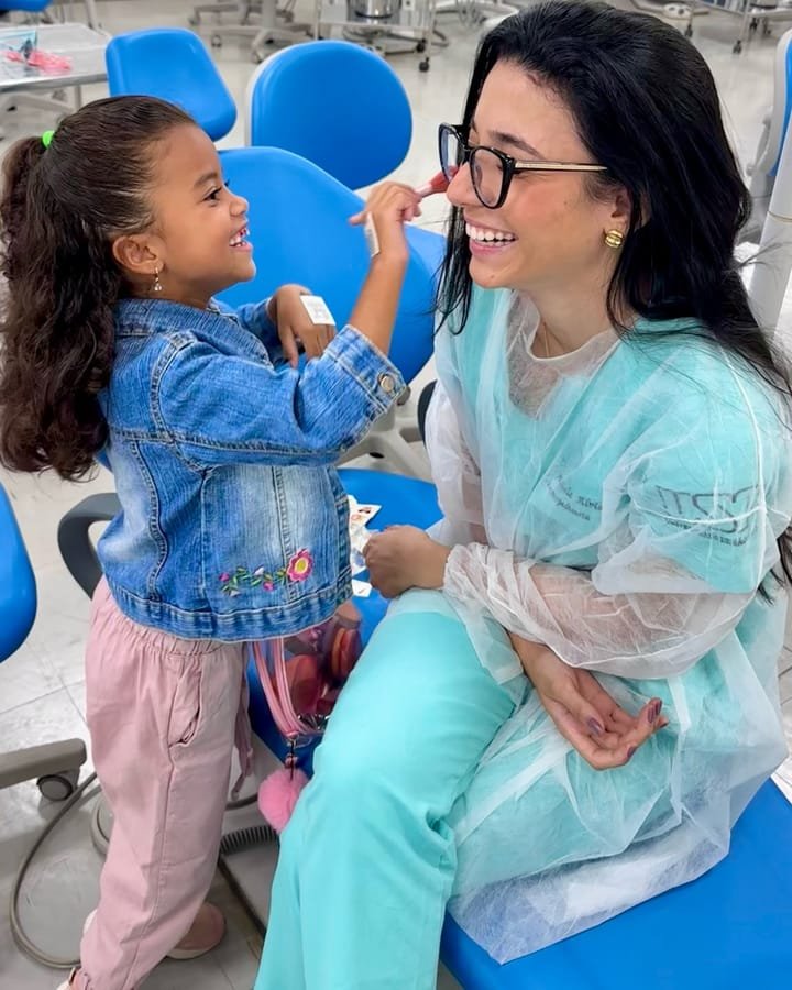 Dra. Graziele Alvim em interação acolhedora com uma criança durante uma atividade educativa de saúde bucal.